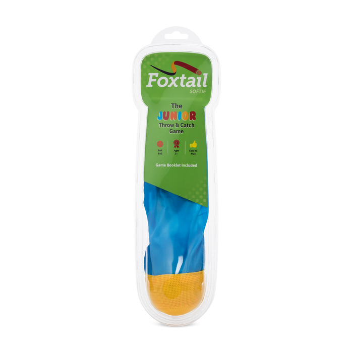 The Foxtail Softie, a yellow ball with a blue fabric tail, comes in clear plastic packaging featuring colorful text on green and white that highlights its fun way to boost hand-eye coordination through safe throwing and catching.